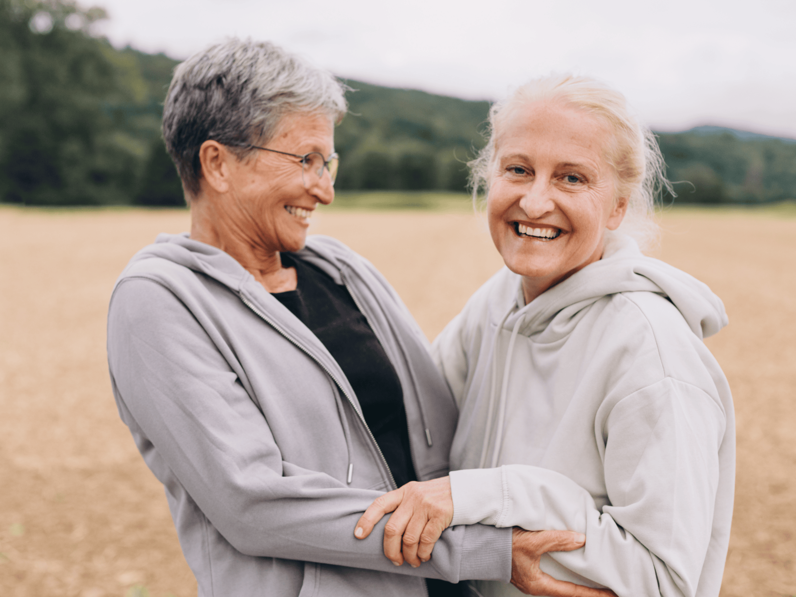 Elderly women smiling and hugging outdoors, representing community, support, and compassion in faith-based initiatives.