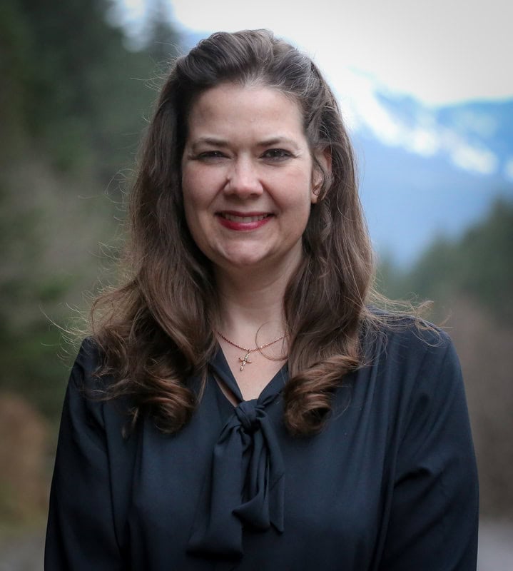 A caring woman from Catholic Community Services stands outdoors in a scenic natural setting, exemplifying compassion and community support.
