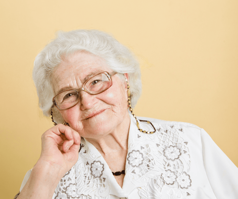 Elderly woman smiling with glasses and white lace blouse, symbolizing compassionate community service.